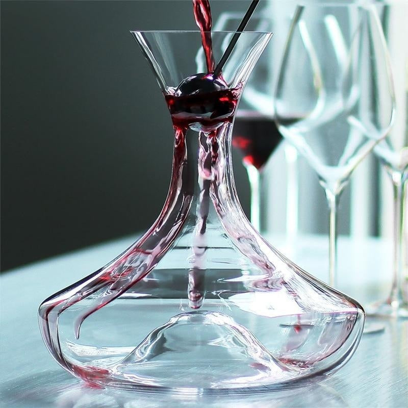 Red wine being poured into a glass decanter on a reflective surface.