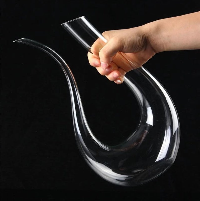 Clear glass decanter held by a hand against a black background
