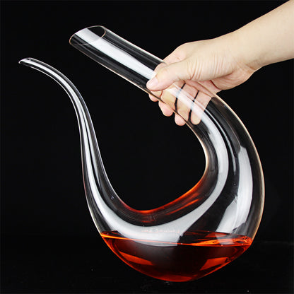 Hand holding a glass wine decanter with red wine against a black background
