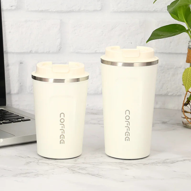 Two white insulated coffee cups with silver lids on a marble surface next to a laptop.