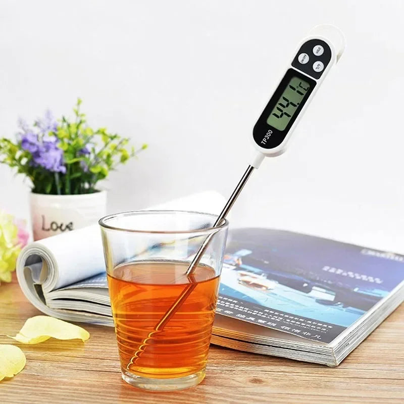 Digital thermometer inserted into a glass of tea on a table with a magazine and plant in the background.
