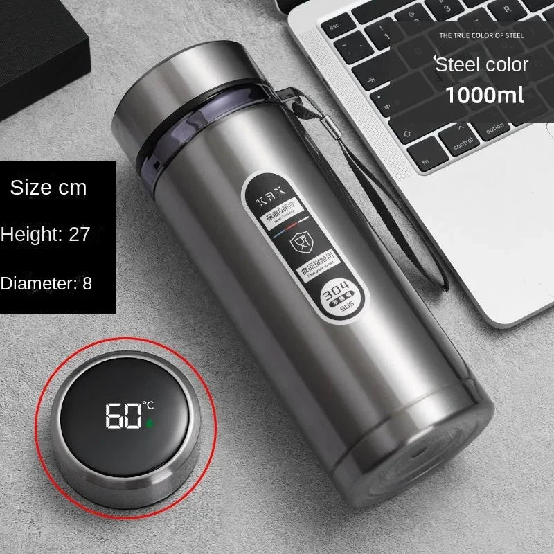 Stainless steel tumbler with digital temperature display on a gray surface next to a laptop.
