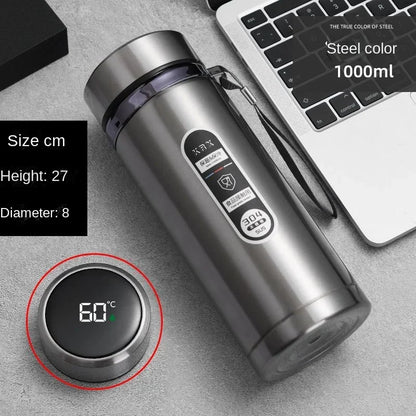 Stainless steel tumbler with digital temperature display on a gray surface next to a laptop.
