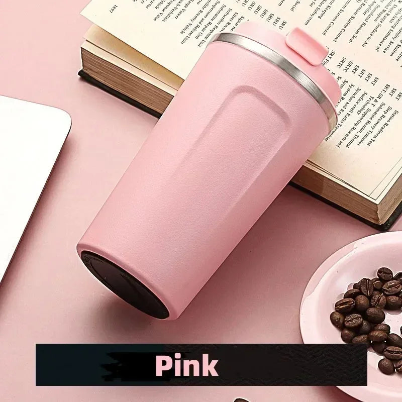 Pink insulated tumbler on a pink surface with coffee beans and an open book.