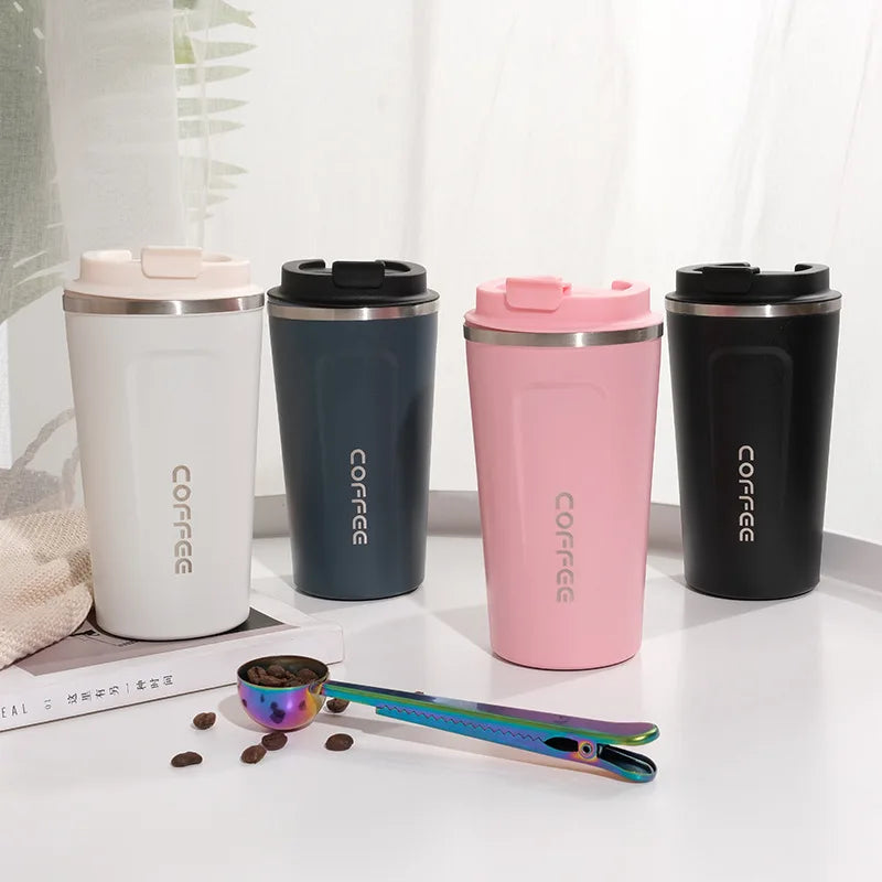 Four stainless steel coffee tumblers in white, navy, pink, and black on a light surface with coffee beans and a scoop.